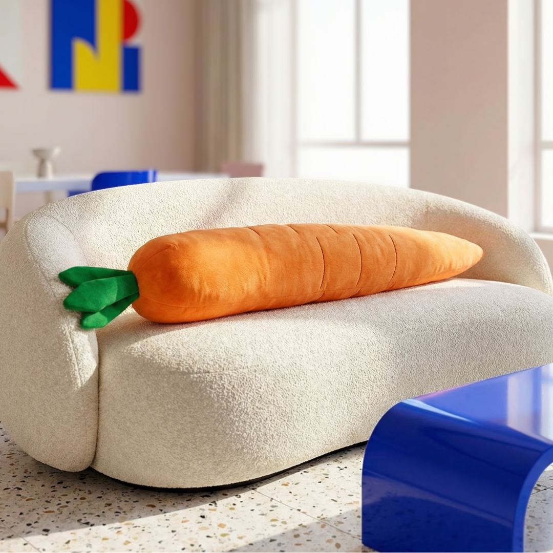 Giant orange plush carrot dog toy with green leafy top resting on a cream-colored sofa.