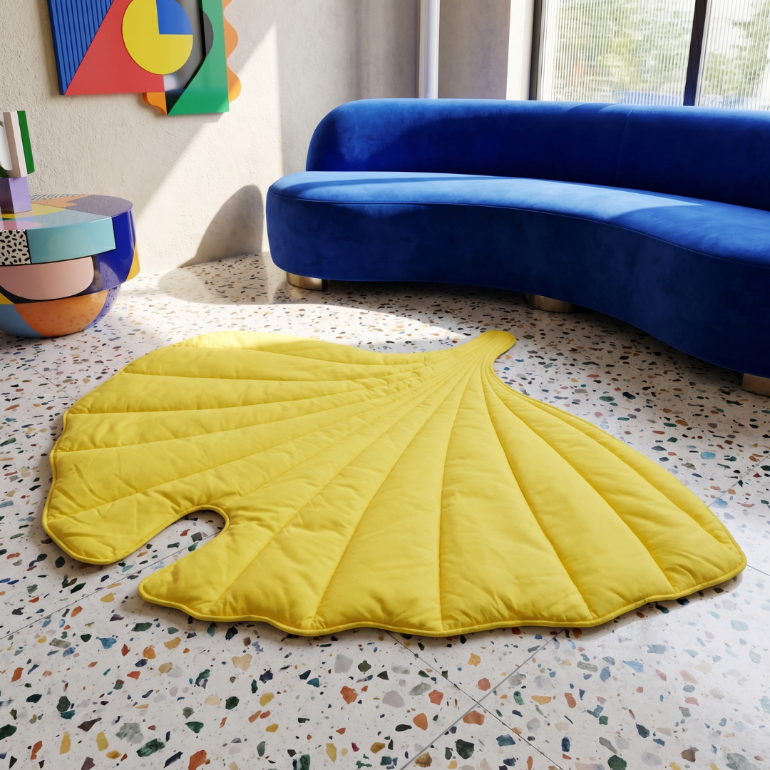 Yellow leaf-shaped calming dog bed mat on a speckled floor, with a blue sofa in the background.