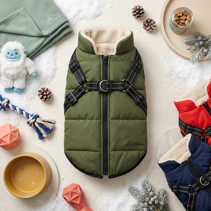 Olive green fleece-lined dog puffer coat with built-in harness, surrounded by winter pet accessories.
